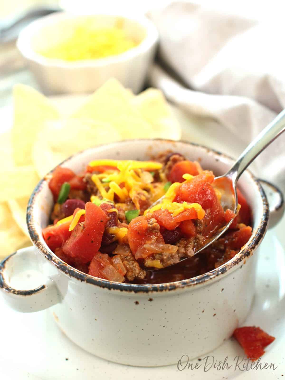 a spoon scooping up chili with tomatoes and shredded cheese.
