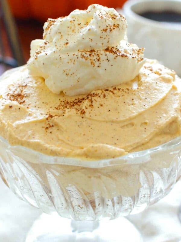 a clear dessert dish with pumpkin cheesecake topped with whipped cream.