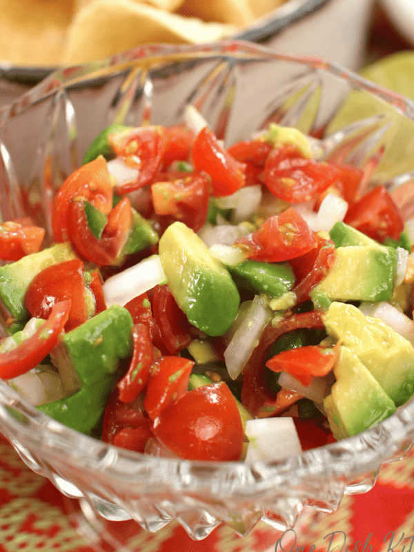 a bowl of pico de gallo with chopped avocados on top surrounded by a red and yellow tablecloth.