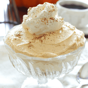 a clear dessert dish with pumpkin cheesecake topped with whipped cream.