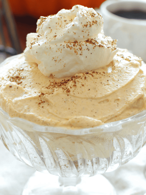 a clear dessert dish with pumpkin cheesecake topped with whipped cream.