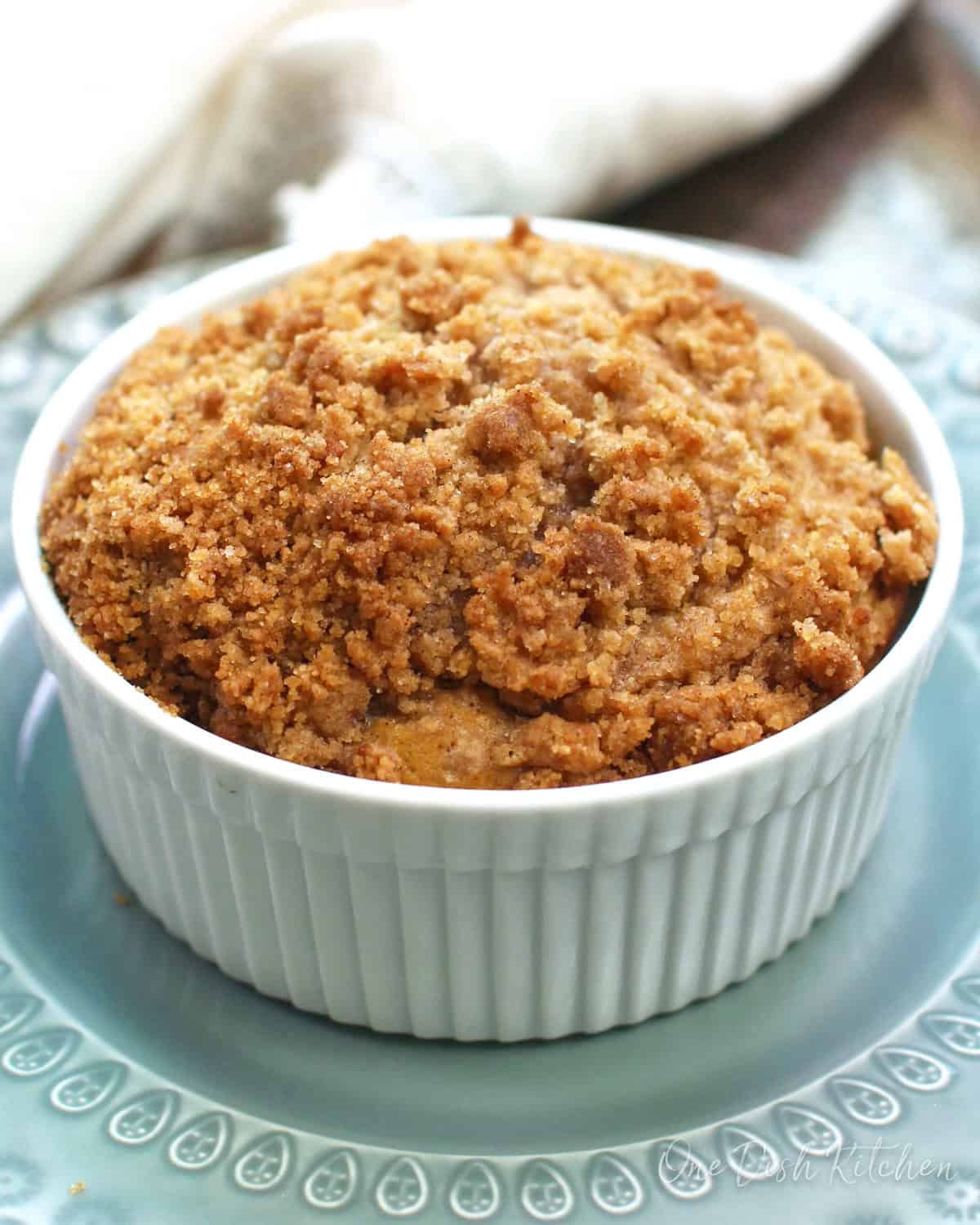 a round coffee cake in a white ramekin sitting on top of a blue plate on a silver tray.