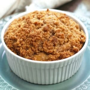 a round coffee cake in a white ramekin sitting on top of a blue plate on a silver tray.