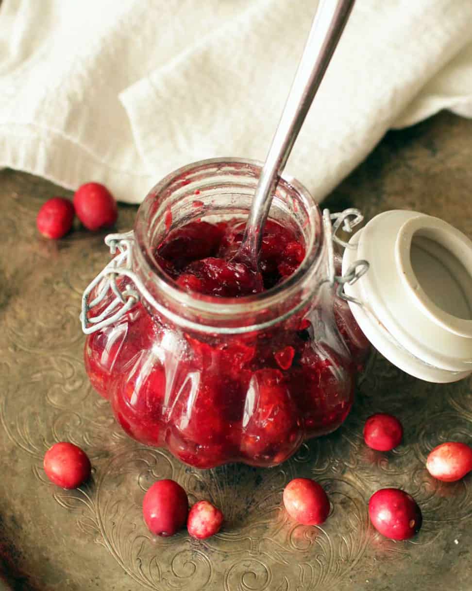 a clear jar of cranberry jam with a spoon sticking out the top.