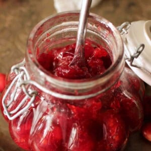 a clear jar of cranberry jam with a spoon sticking out the top.