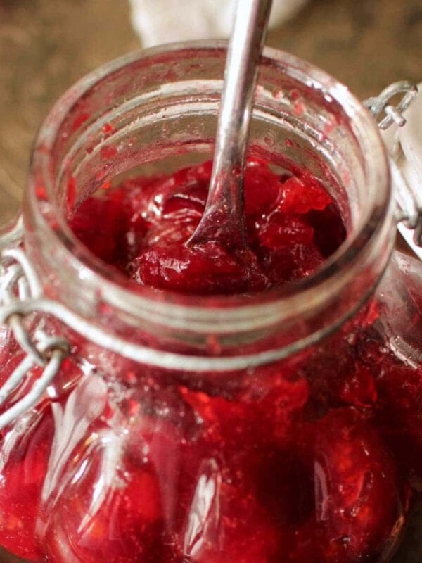 a clear jar of cranberry jam with a spoon sticking out the top.