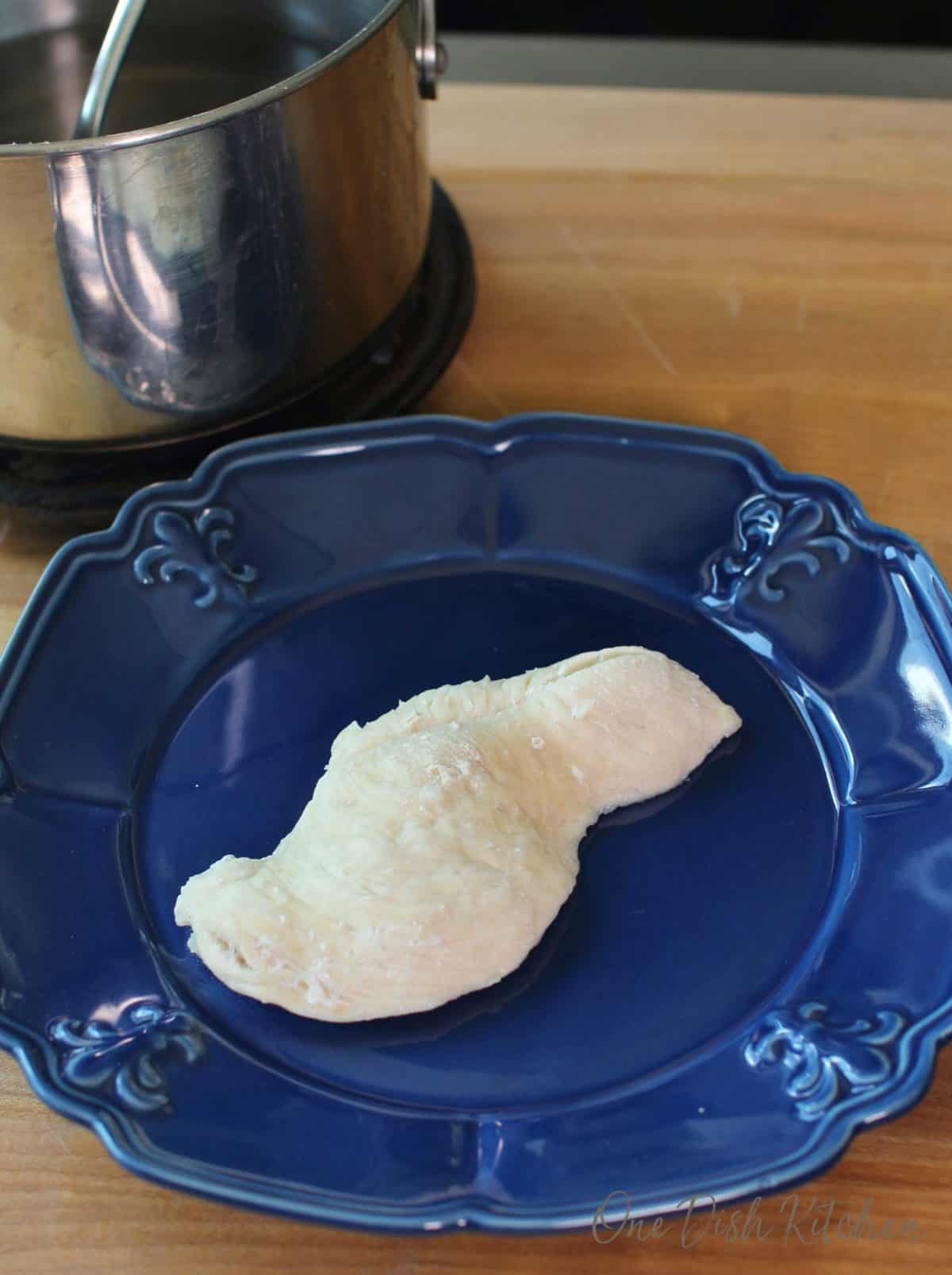 a piece of chicken on a blue plate next to a silver pot.