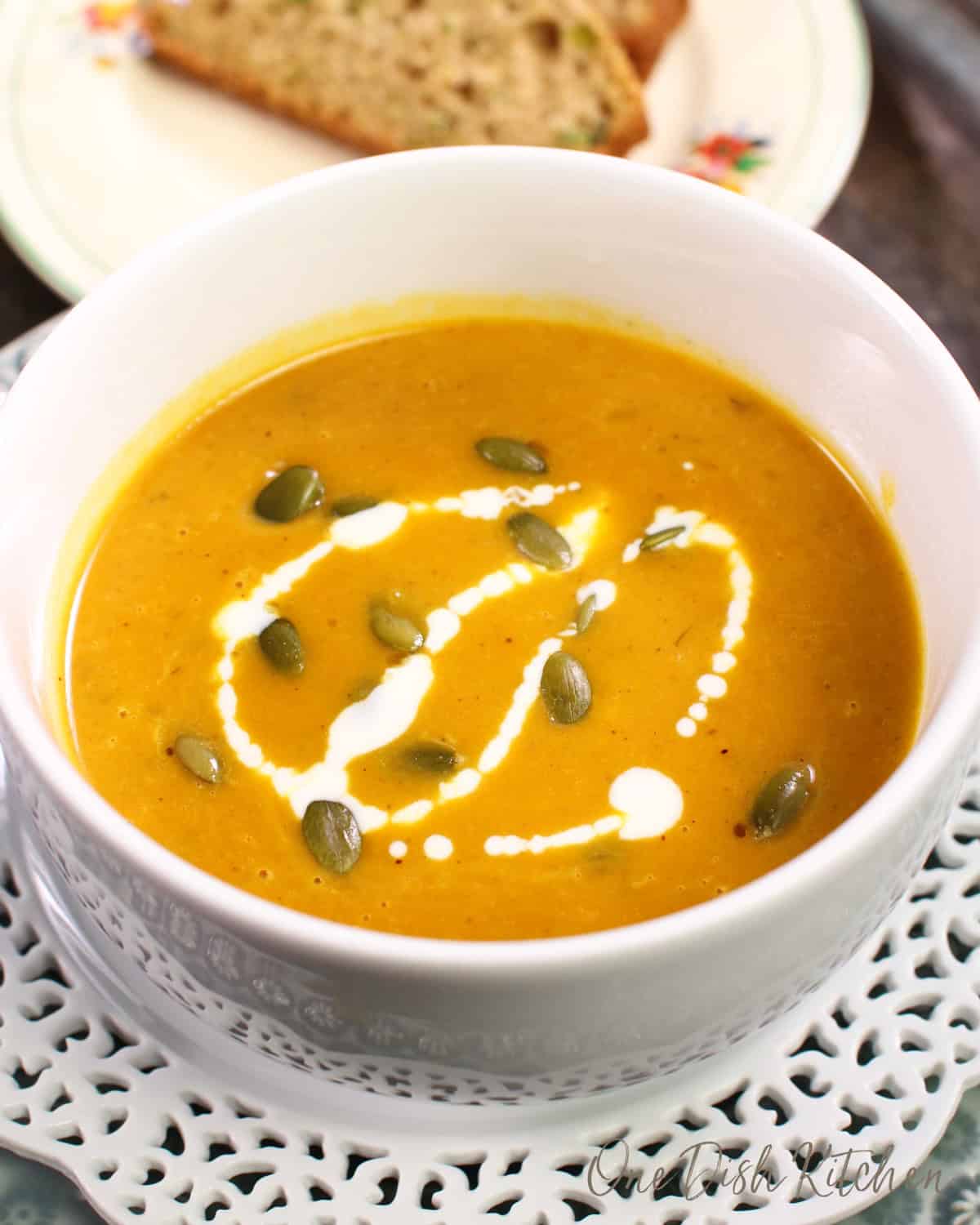 pumpkin soup in a white bowl topped with pumpkin seeds and a drizzle of cream.