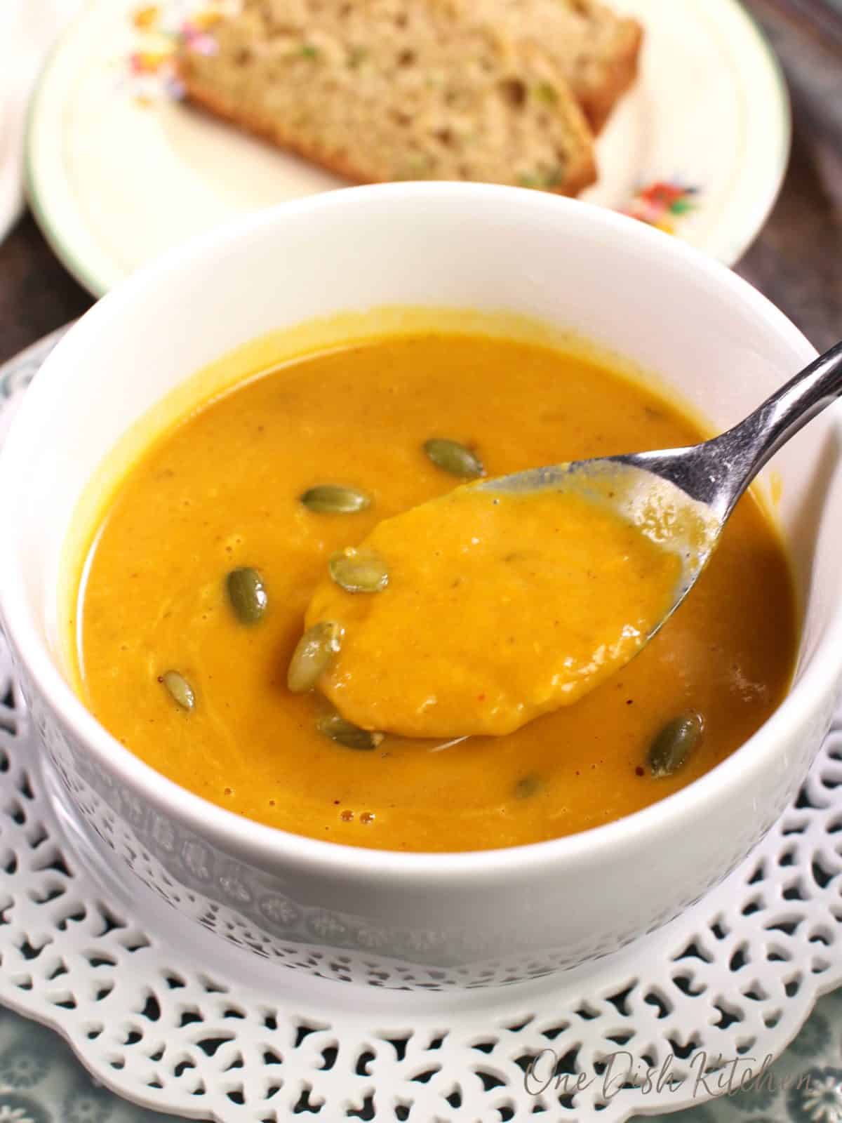 a bowl of pumpkin soup with a spoonful next to the bowl.