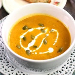 pumpkin soup in a white bowl topped with pumpkin seeds and a drizzle of cream