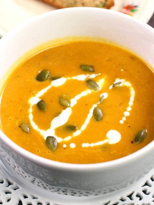 pumpkin soup in a white bowl topped with pumpkin seeds and a drizzle of cream
