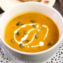 pumpkin soup in a white bowl topped with pumpkin seeds and a drizzle of cream.