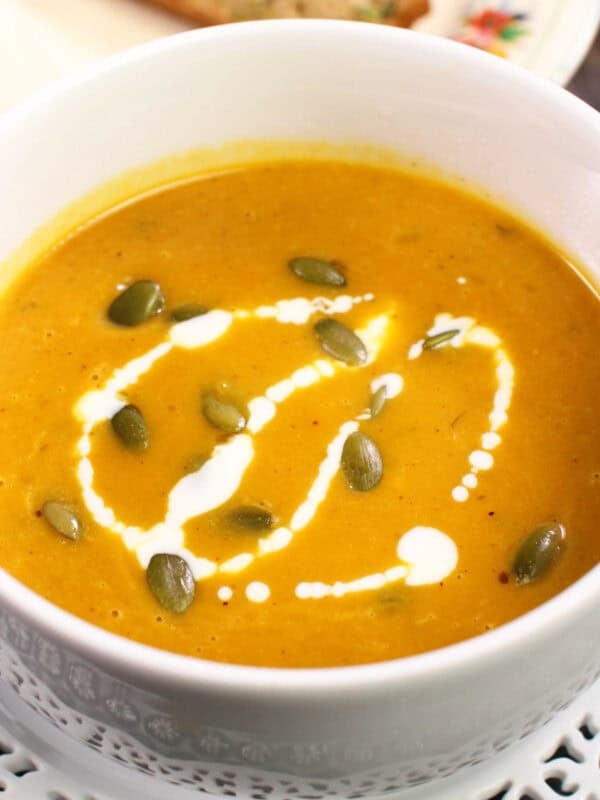 pumpkin soup in a white bowl topped with pumpkin seeds and a drizzle of cream.