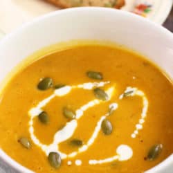 a bowl of pumpkin soup topped with cream and pumpkin seeds.