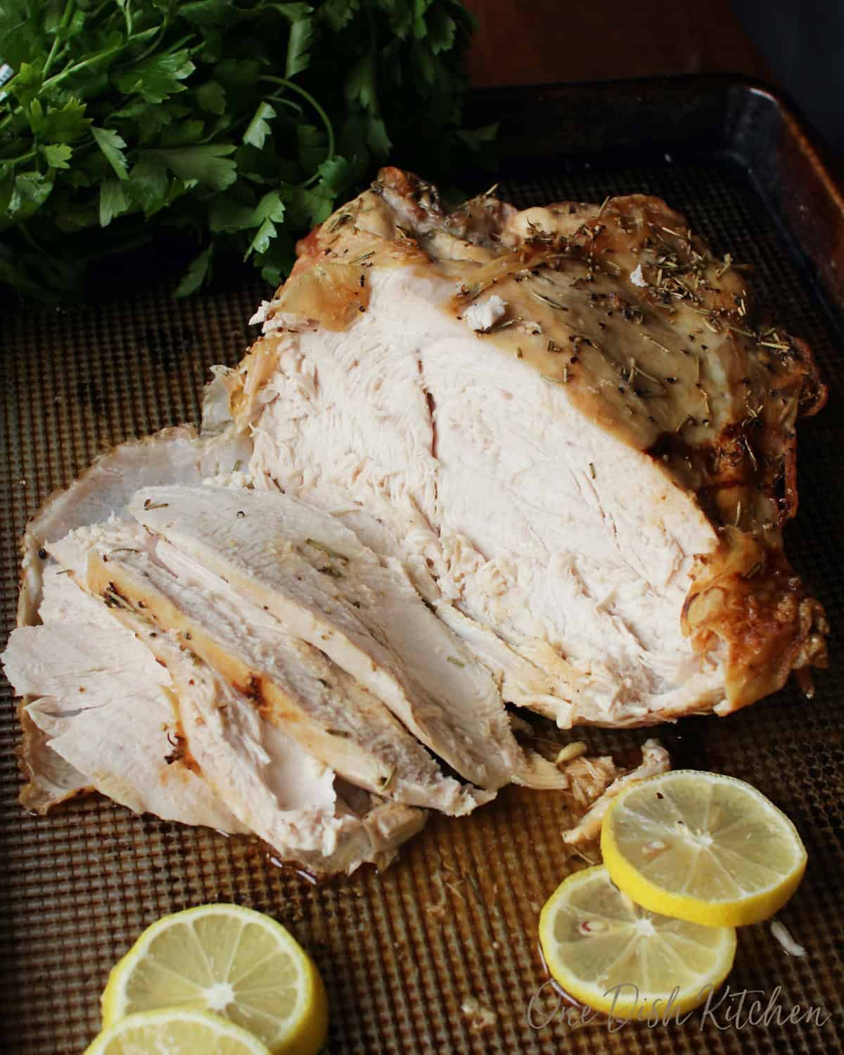 a roast split turkey breast on a baking sheet with slices of lemon.