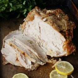 a roast turkey breast on a baking sheet partially sliced next to lemons