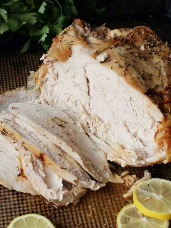 a roast turkey breast on a baking sheet partially sliced next to lemons
