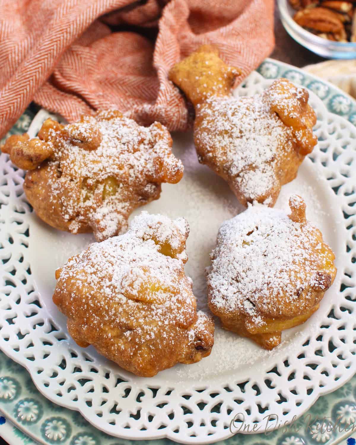 four crispy apple fritters topped with powdered sugar on a white plate.