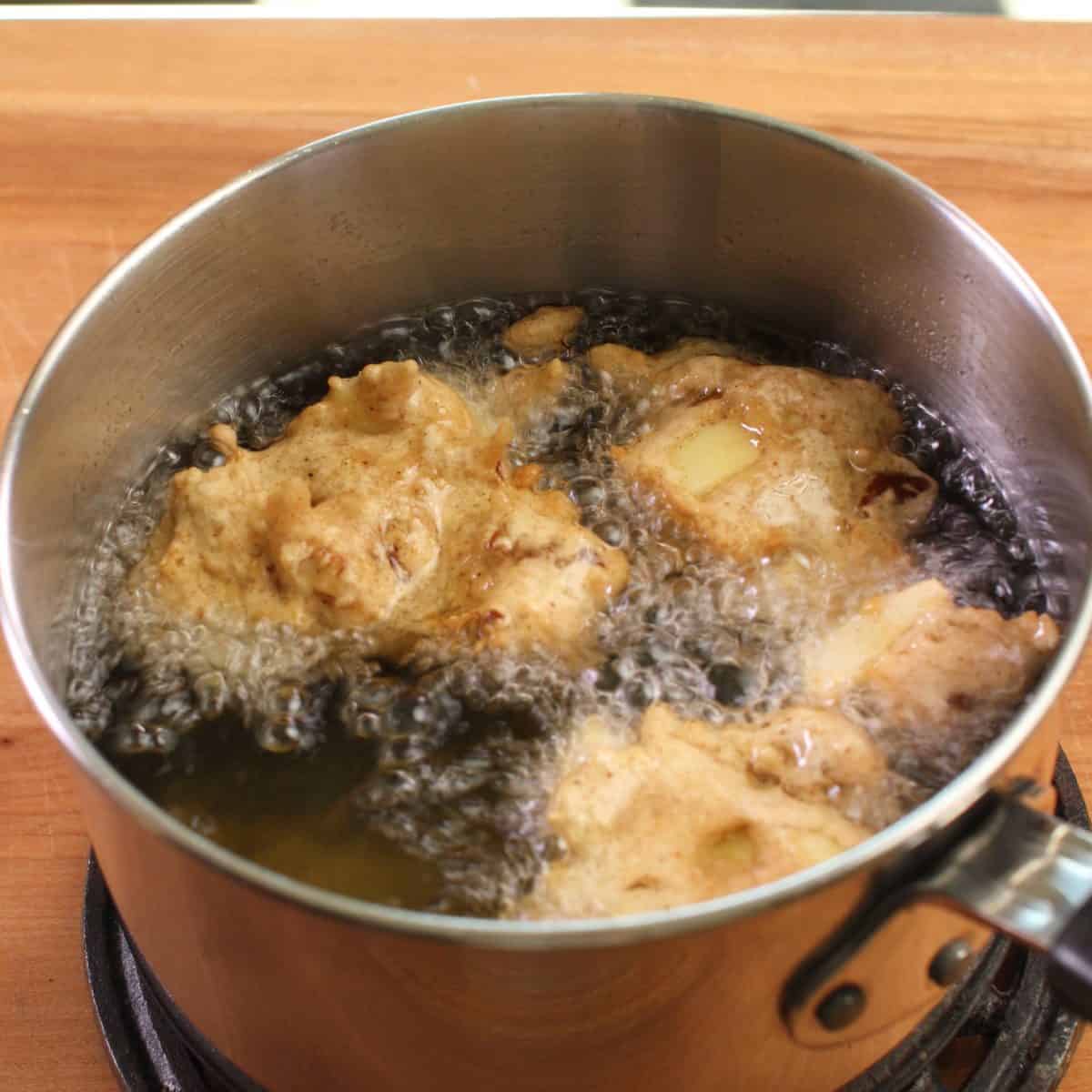 four fritters frying in hot oil in a small pot.
