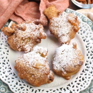 four apple fritters topped with powdered sugar on a white plate