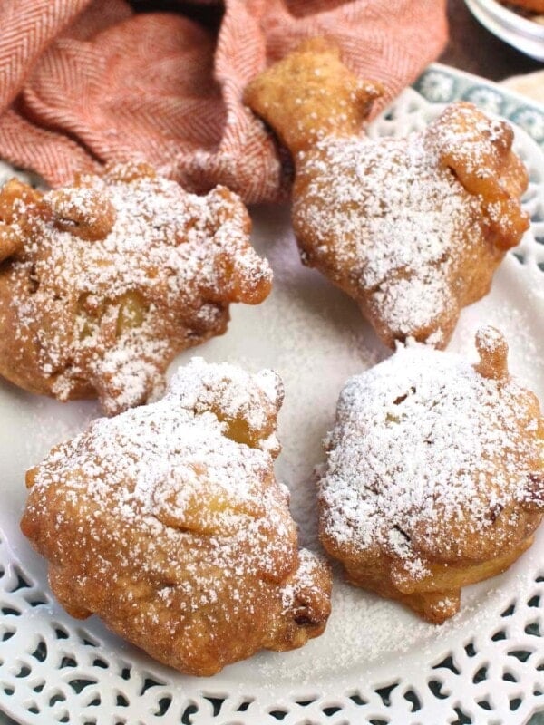 four apple fritters topped with powdered sugar on a white plate