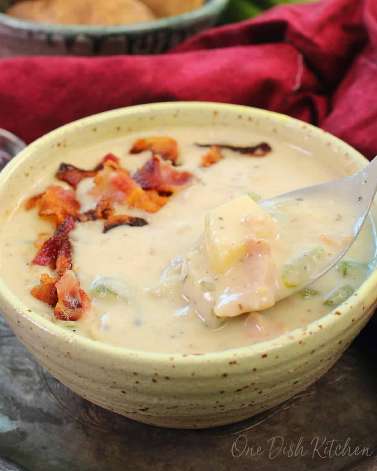 a yellow bowl of clam chowder on a tray next to a red napkin.