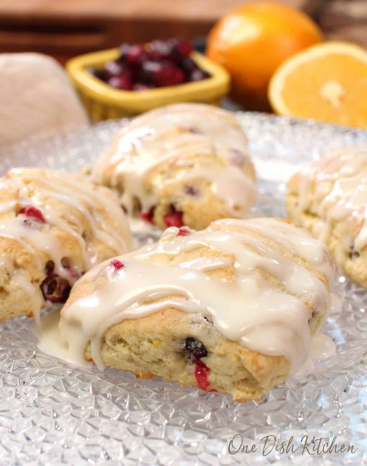 cranberry orange scones on a clear plate next to a bowl of fresh cranberries.