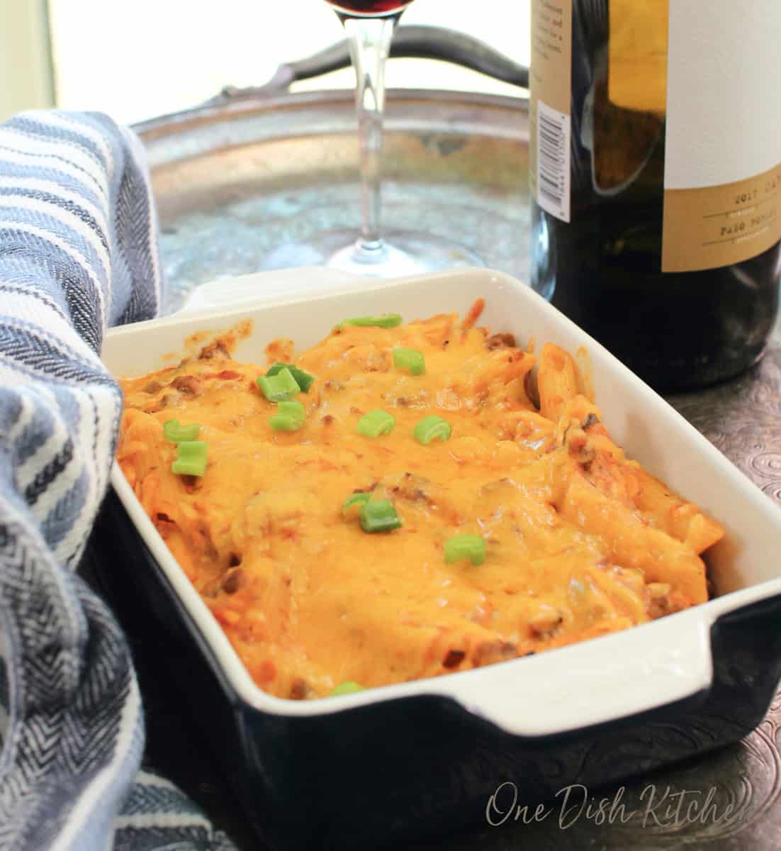 a mini hamburger casserole on a silver tray next to a bottle of red wine.