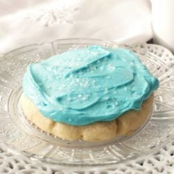 a soft frosted sugar cookie on a white plate next to a white napkin