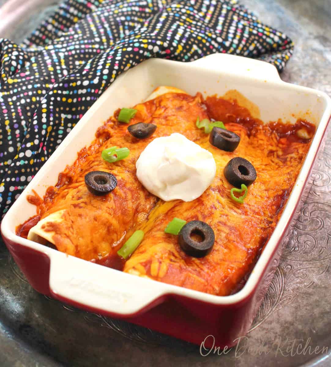 two beef enchiladas in a red baking dish.