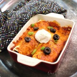 a rectangular baking dish filled with two enchiladas topped with sour cream.