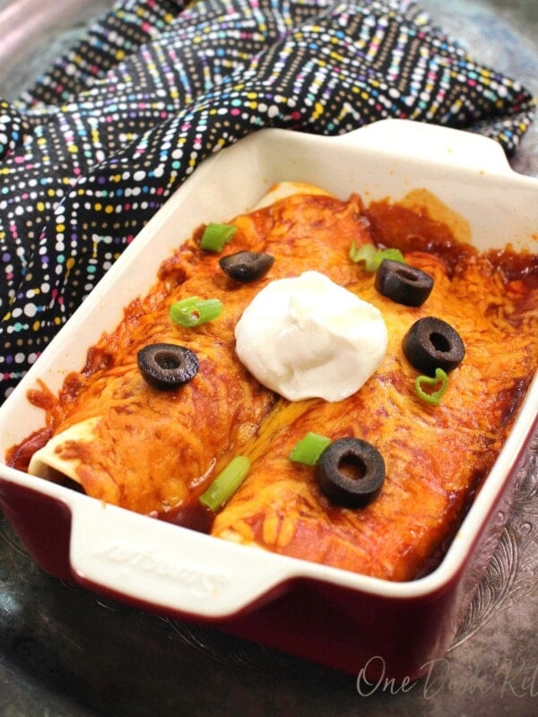 a rectangular baking dish filled with two enchiladas topped with sour cream.