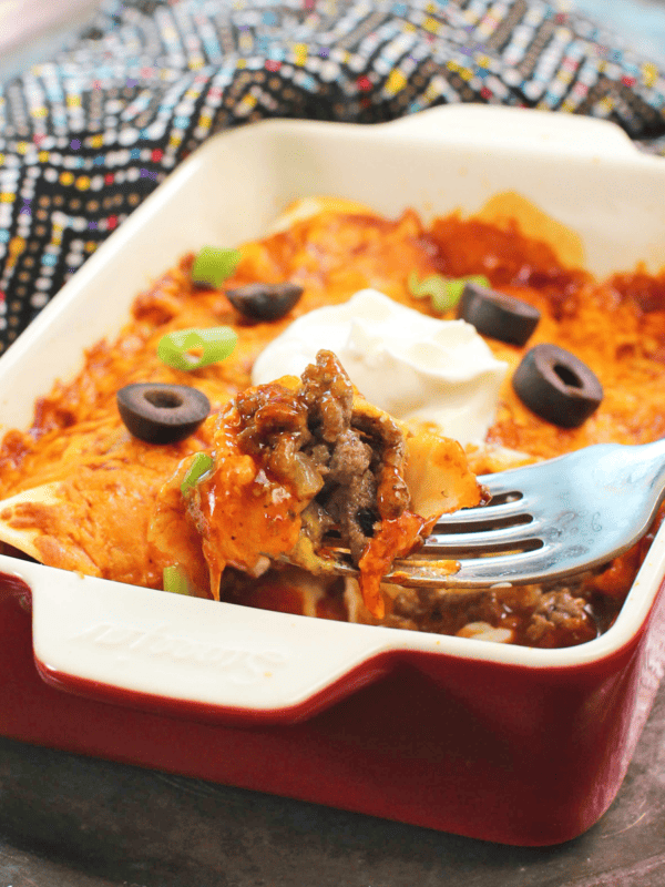 two beef enchiladas in a red dish with a fork on the side of the dish filled with ground beef.