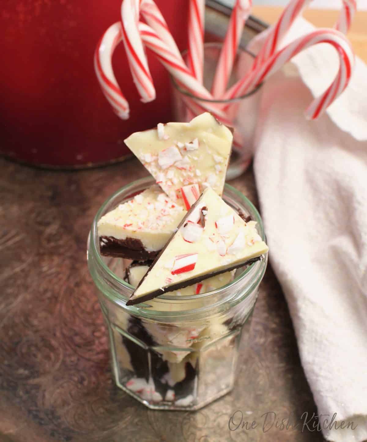 a jar filled with peppermint bark next to candy canes in a jar.