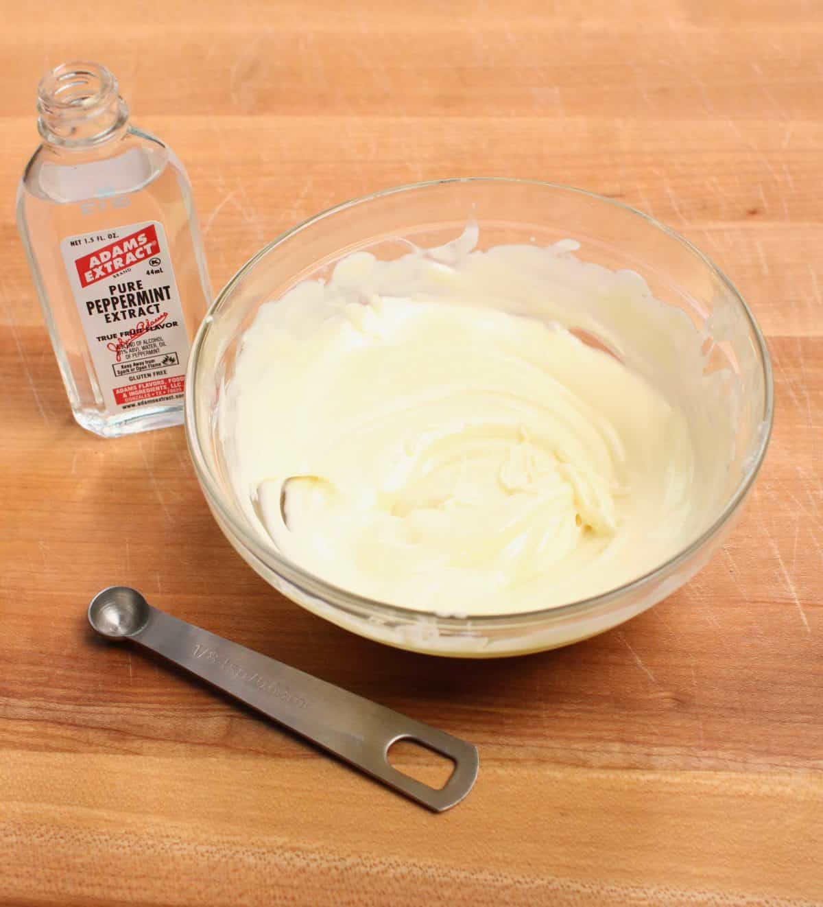 a bowl of white chocolate and a jar of peppermint extract on a brown table.