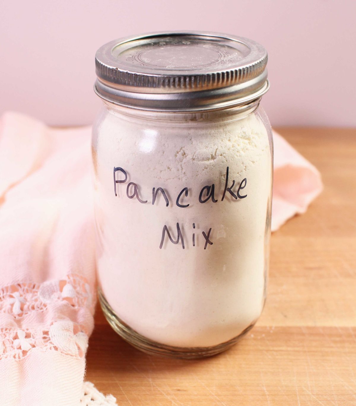 a jar of pancake mix on a brown table next to a pink napkin.