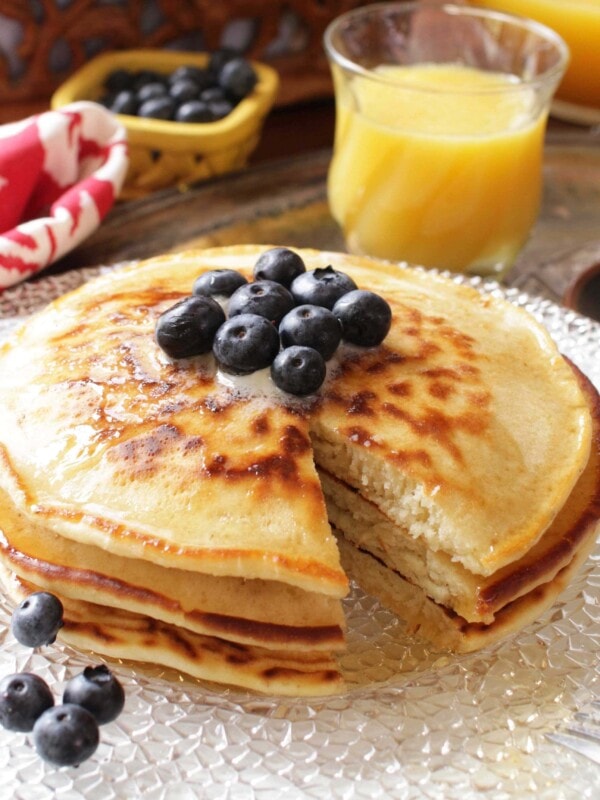 three pancakes on a white plate with blueberries on top and scattered around the plate.
