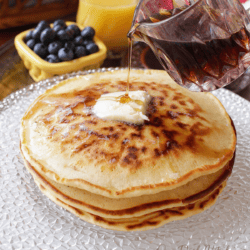 a stack of three pancakes topped with butter next to a bowl of blueberries.