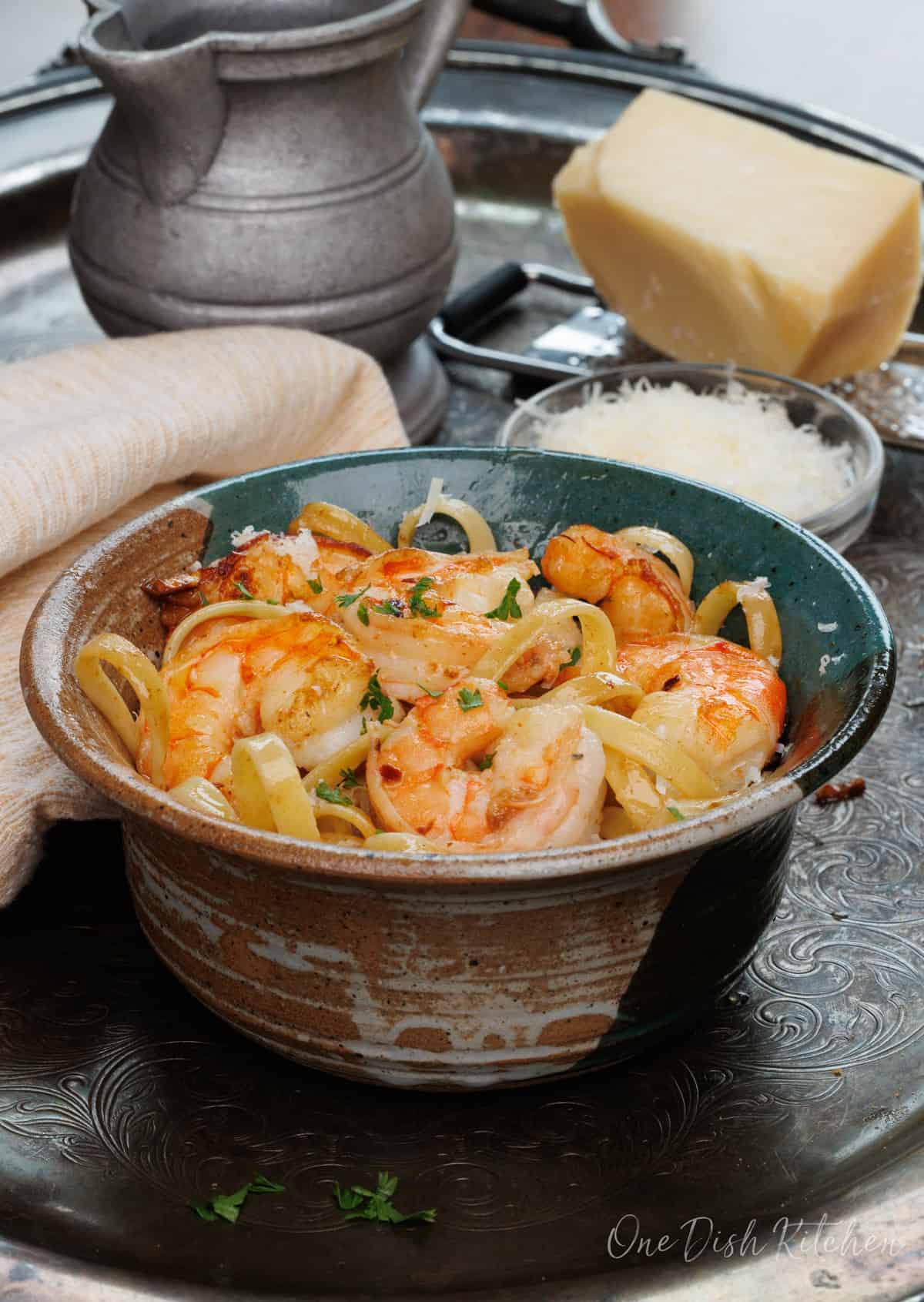 a bowl of shrimp fettuccine on a silver tray next to a fresh block of parmesan cheese.