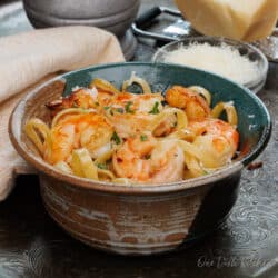 a bowl of shrimp fettuccine on a silver tray next to a fresh block of parmesan cheese