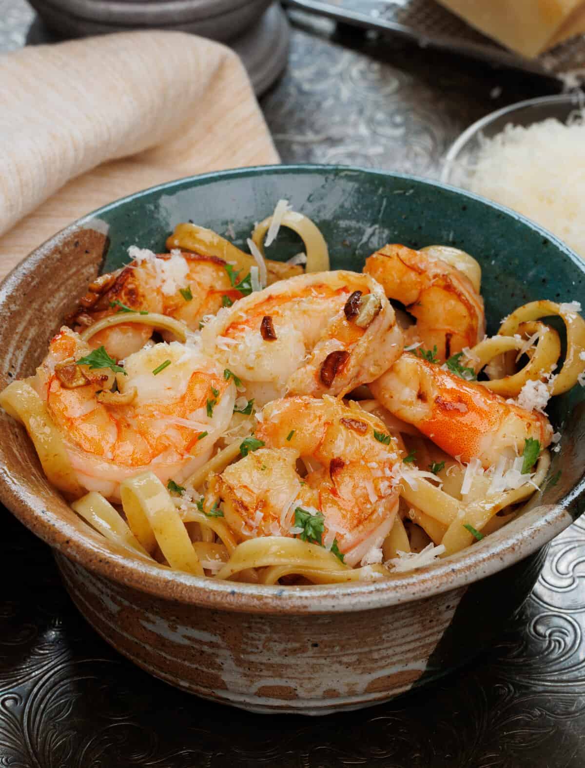 a bowl of shrimp and pasta next to a tan napkin.