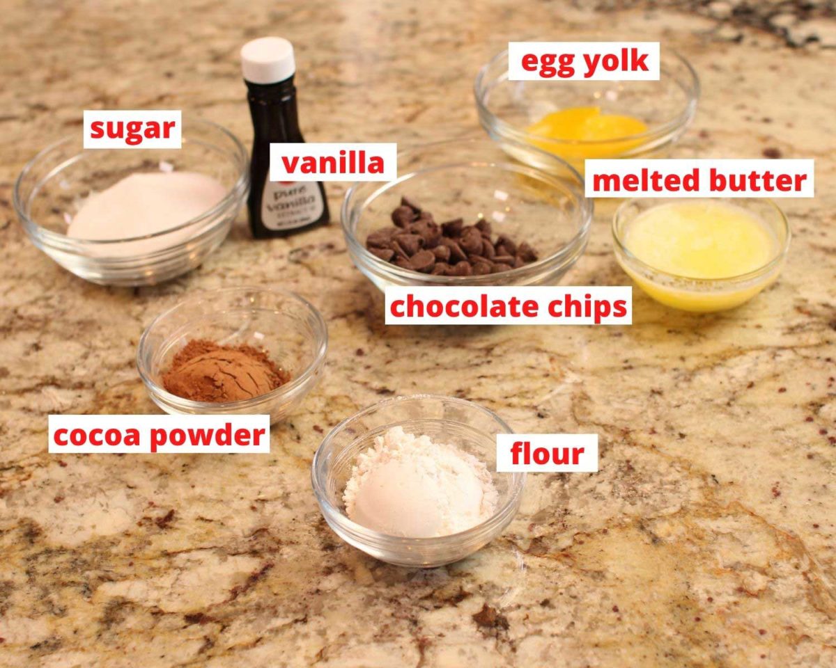 flour, chocolate chips, cocoa powder, butter, vanilla, and egg in individual bowl on a granite countertop.
