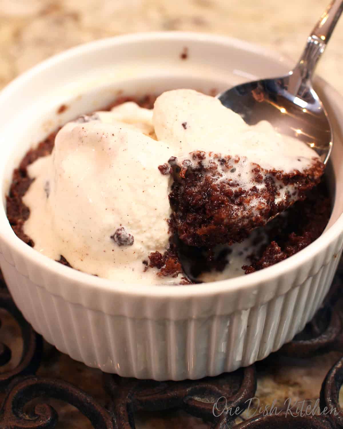 a fudgy brownie in a ramekin with ice cream and a spoon on the side.