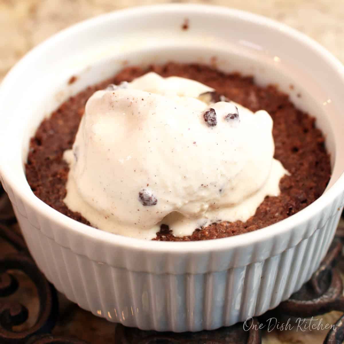 a single brownie in a white ramekin topped with ice cream.