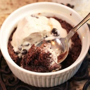 a single serve fudgy brownie topped with ice cream and a spoon on the side.