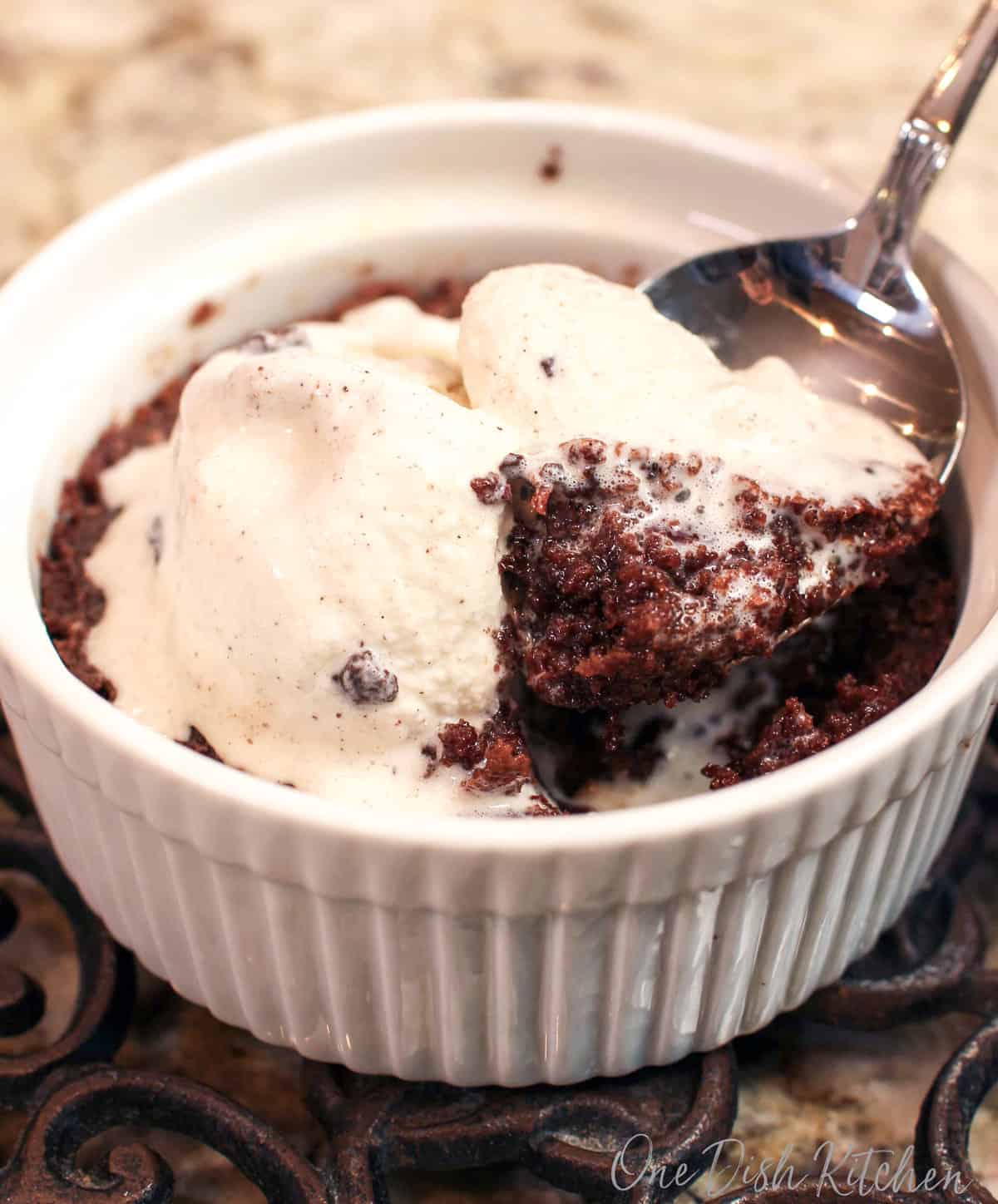 a deep dish brownie topped with ice cream and a spoon in the center.