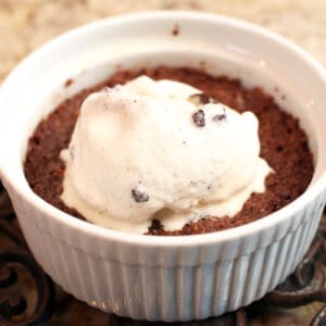 a brownie in a white round dish with ice cream on top