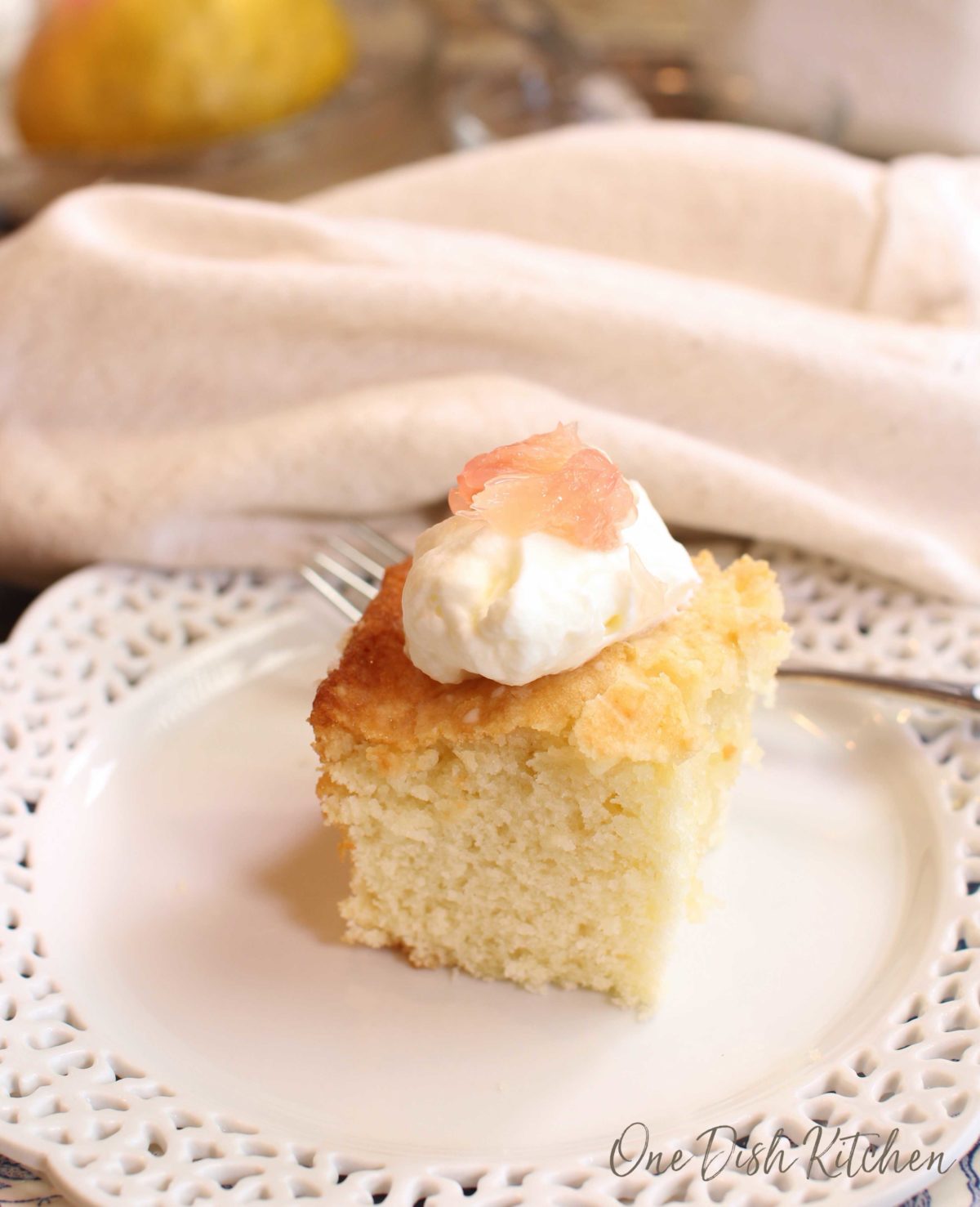 a square piece of cake topped with whipped cream and fresh grapefruit.
