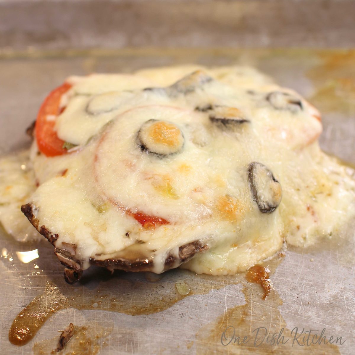 a single mushroom pizza on a baking sheet with melted cheese covering the edges of the crust.