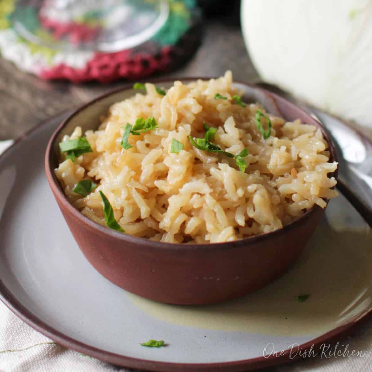 a single serving of rice pilaf in a bowl next to half of an onion.
